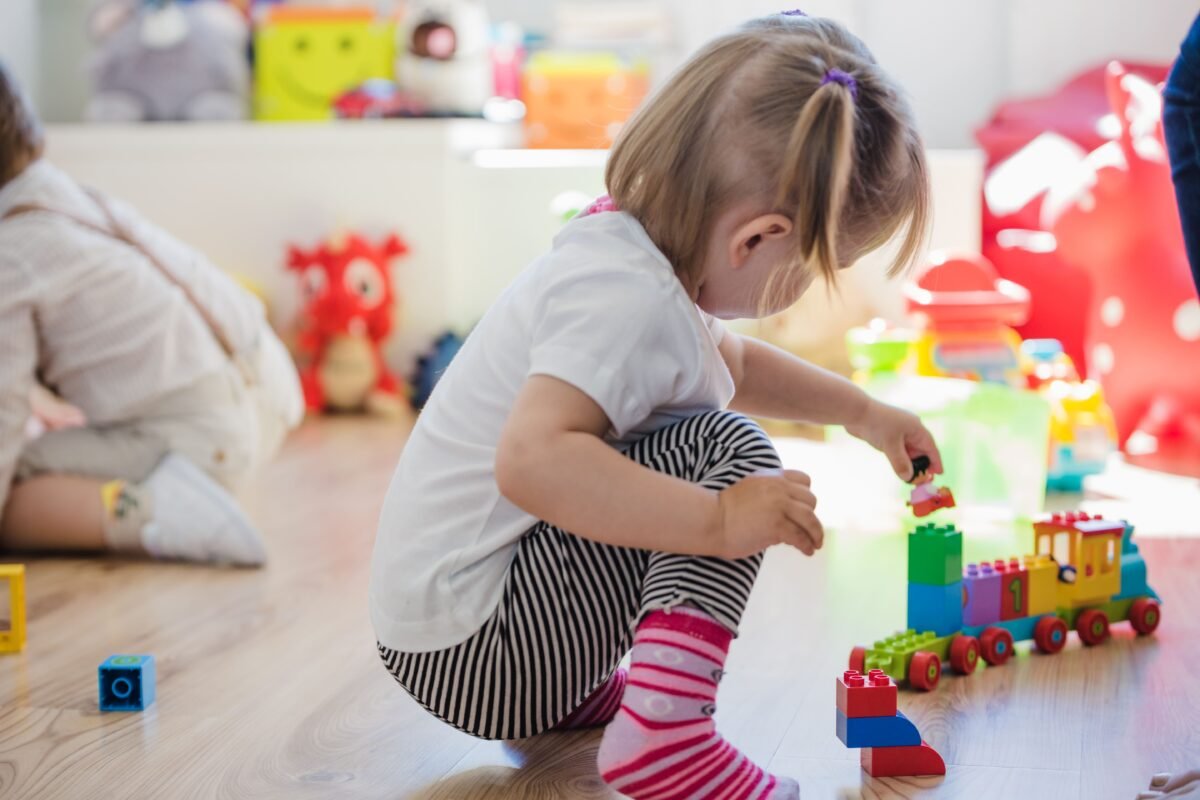 Niña agachada jugando con un tren de piezas de construcción de colores